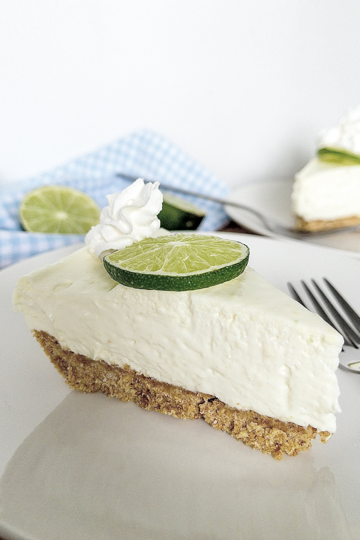 A slice of no bake key lime pie on a white plate with another slice in the background. 