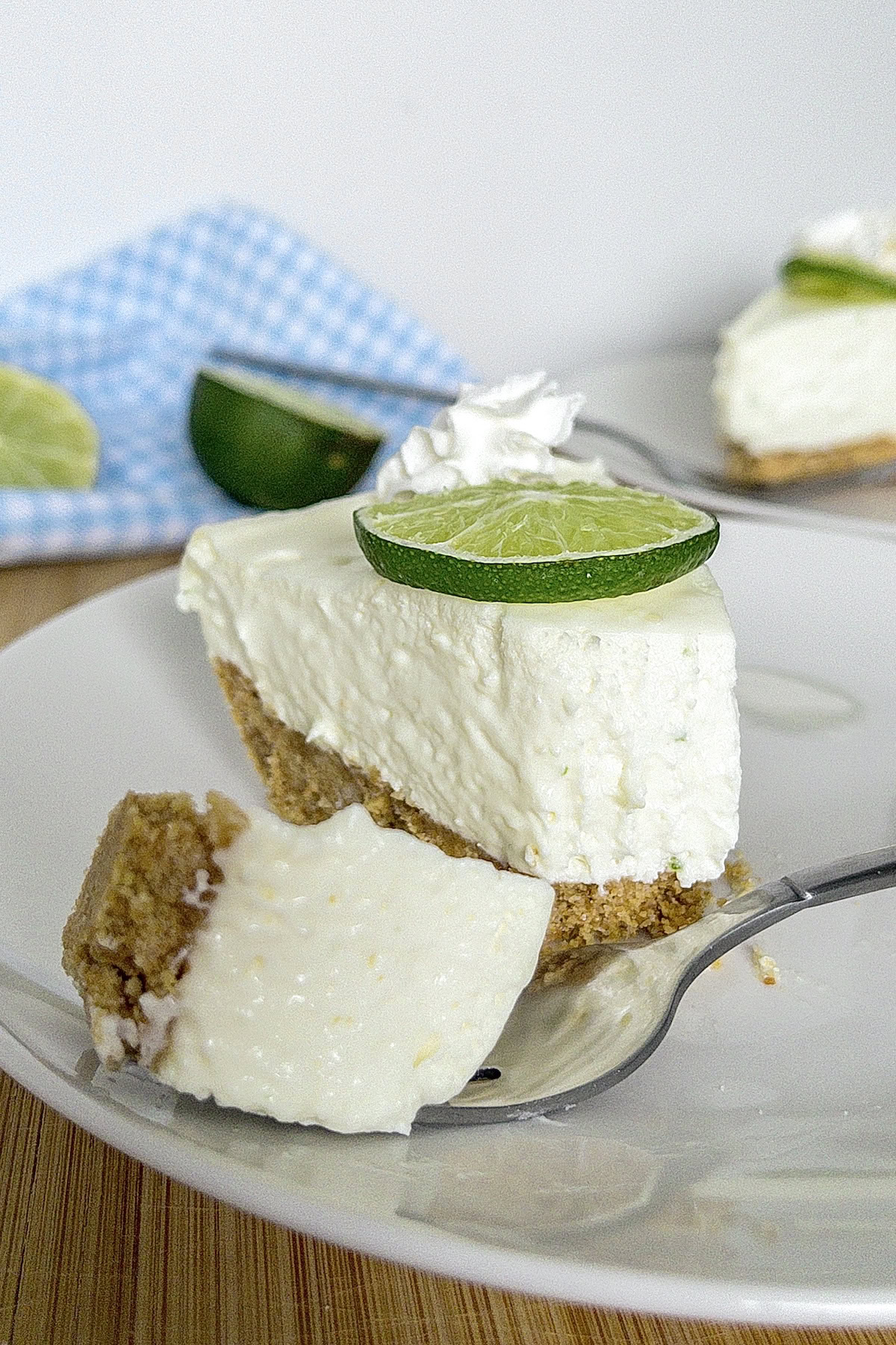 A slice of no bake key lime pie on a white plate with a bite taken from it with another slice in the background. 