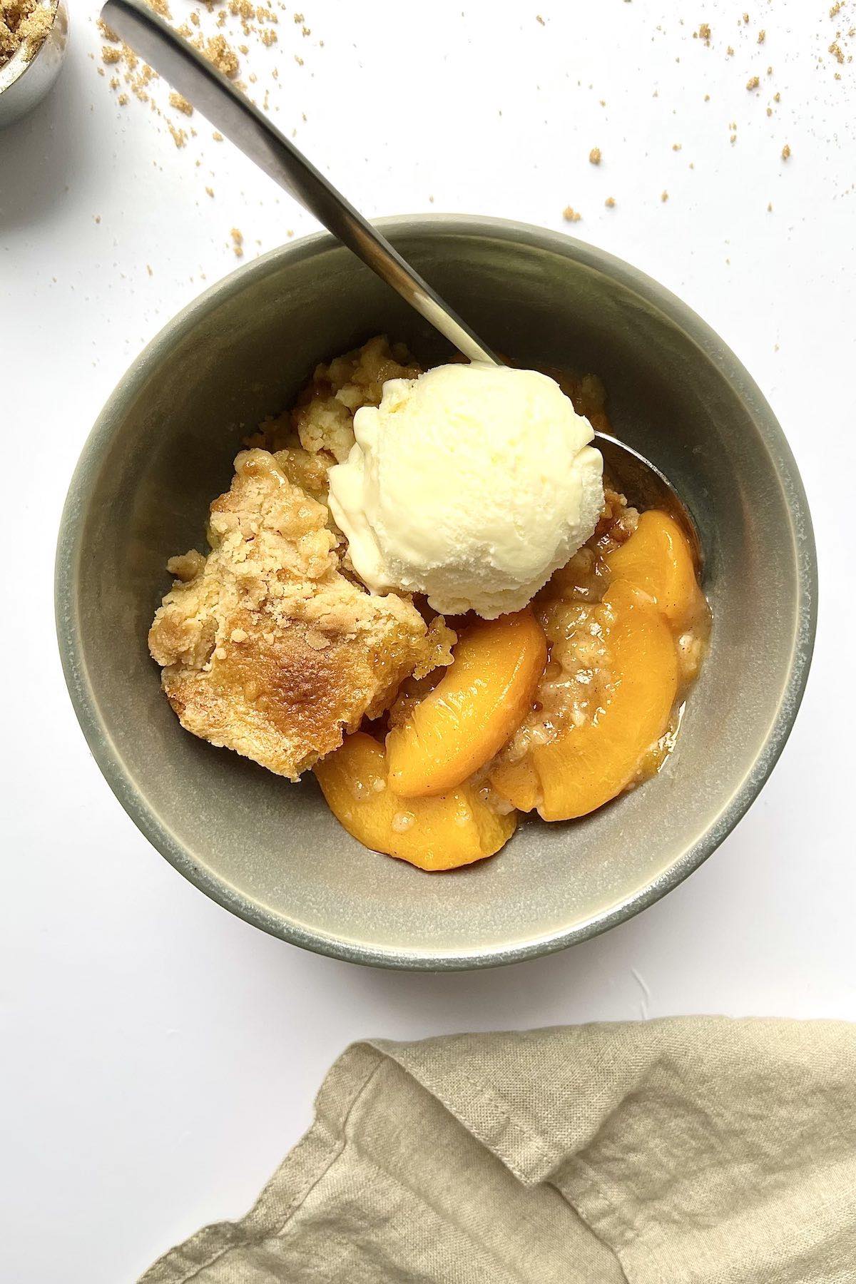Peach cobbler in a bowl topped with a scoop of vanilla ice cream.