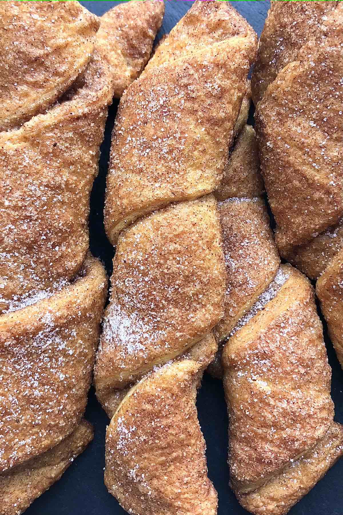 Pumpkin pie twists stacked on a black cutting board. 