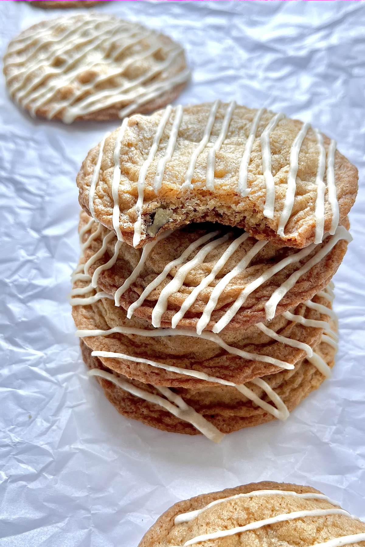 A stack of four chewy maple walnut cookies on a piece of parchment paper with more cookies in the background.