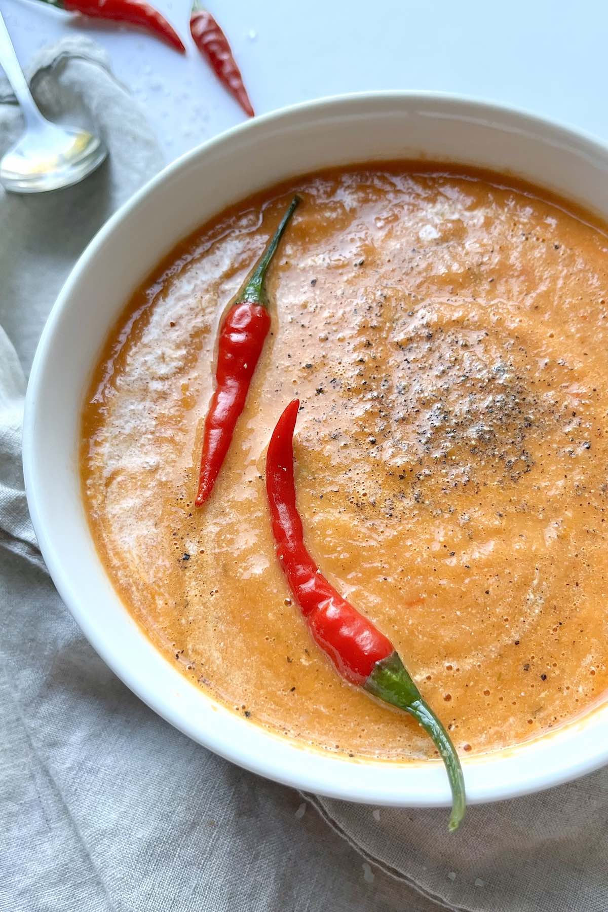Easy blender tomato soup in a white bowl with two fresh red chili peppers in it.