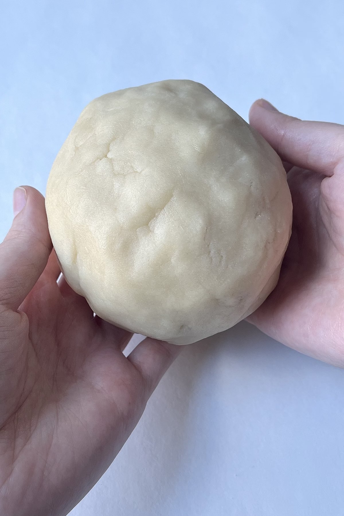 Hands holding cooking dough thats been shaped into a ball.