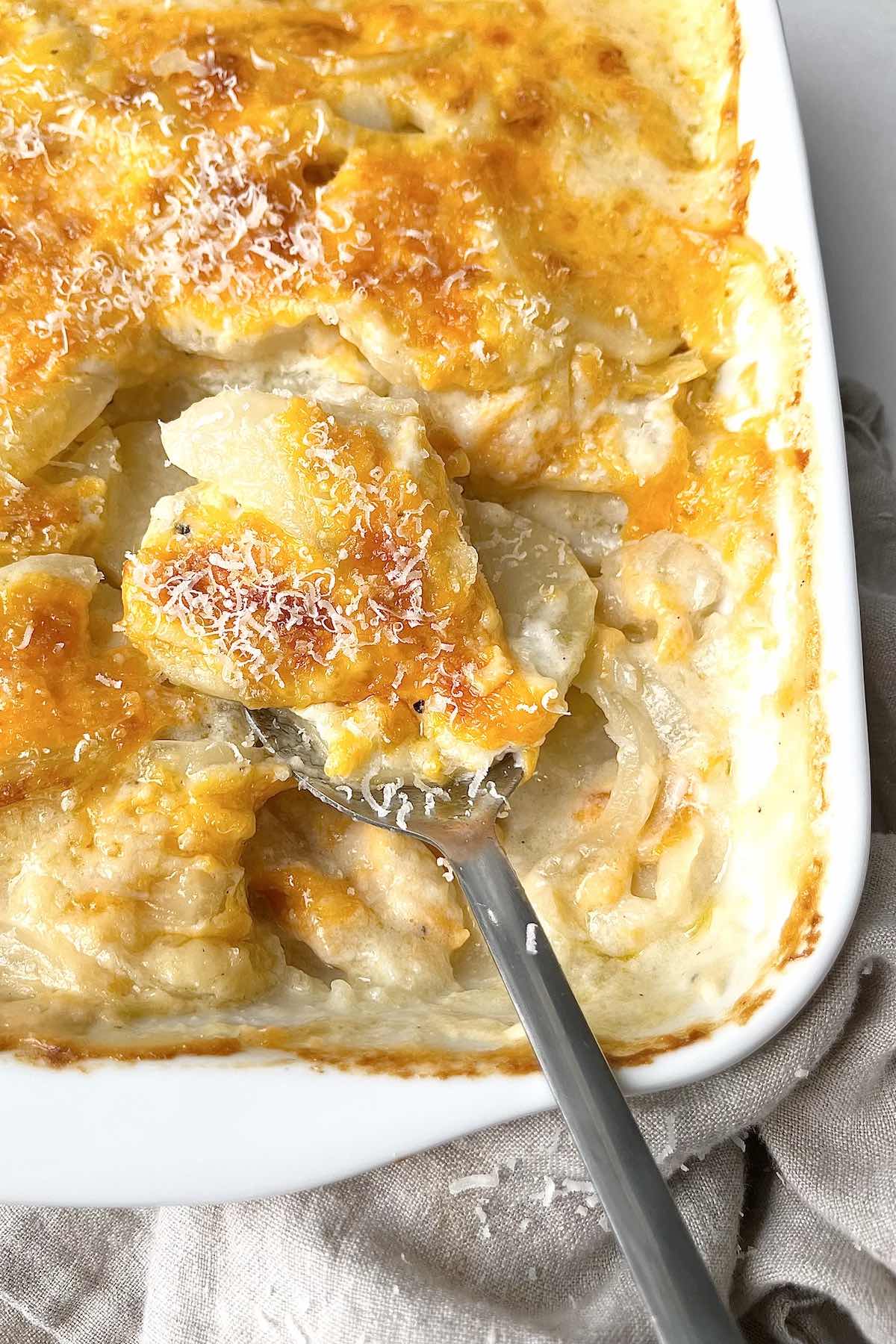 Spoon taking a scoop from a dish of mom's old fashioned scalloped potatoes.