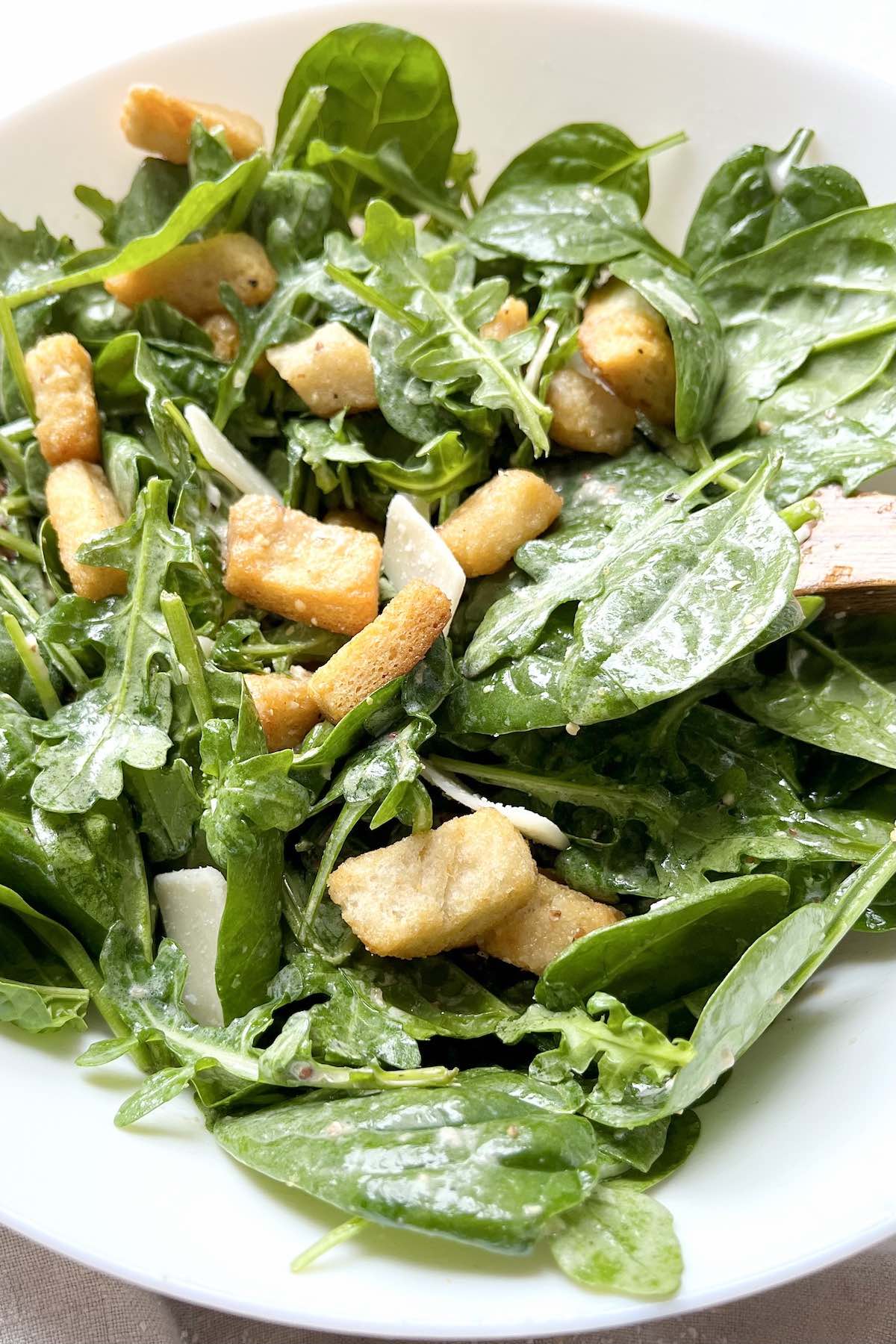 Peppery greens salad in a white bowl with a wooden spoon in it.
