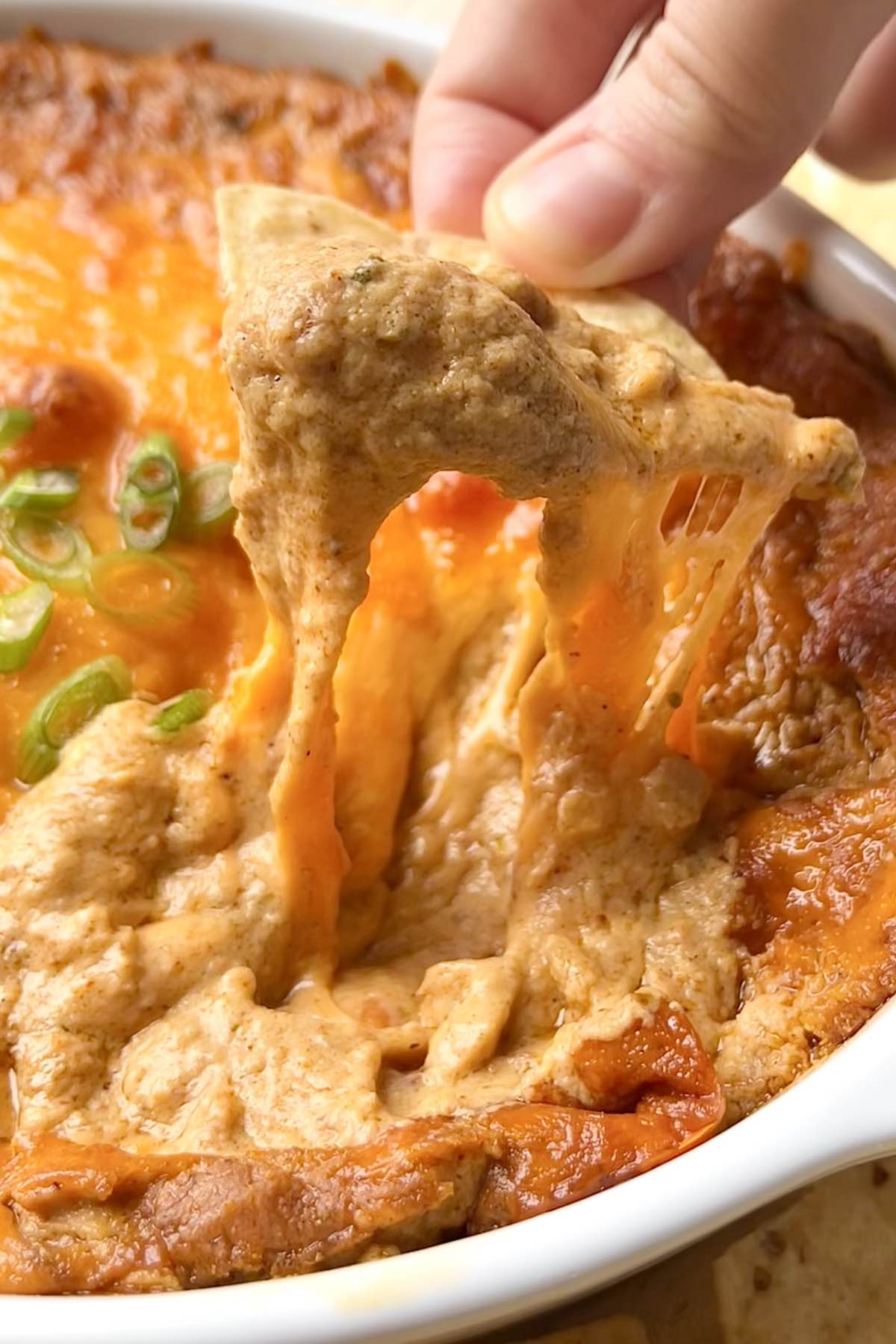 A tortilla chip dipped in bean dip with a cheese pull.