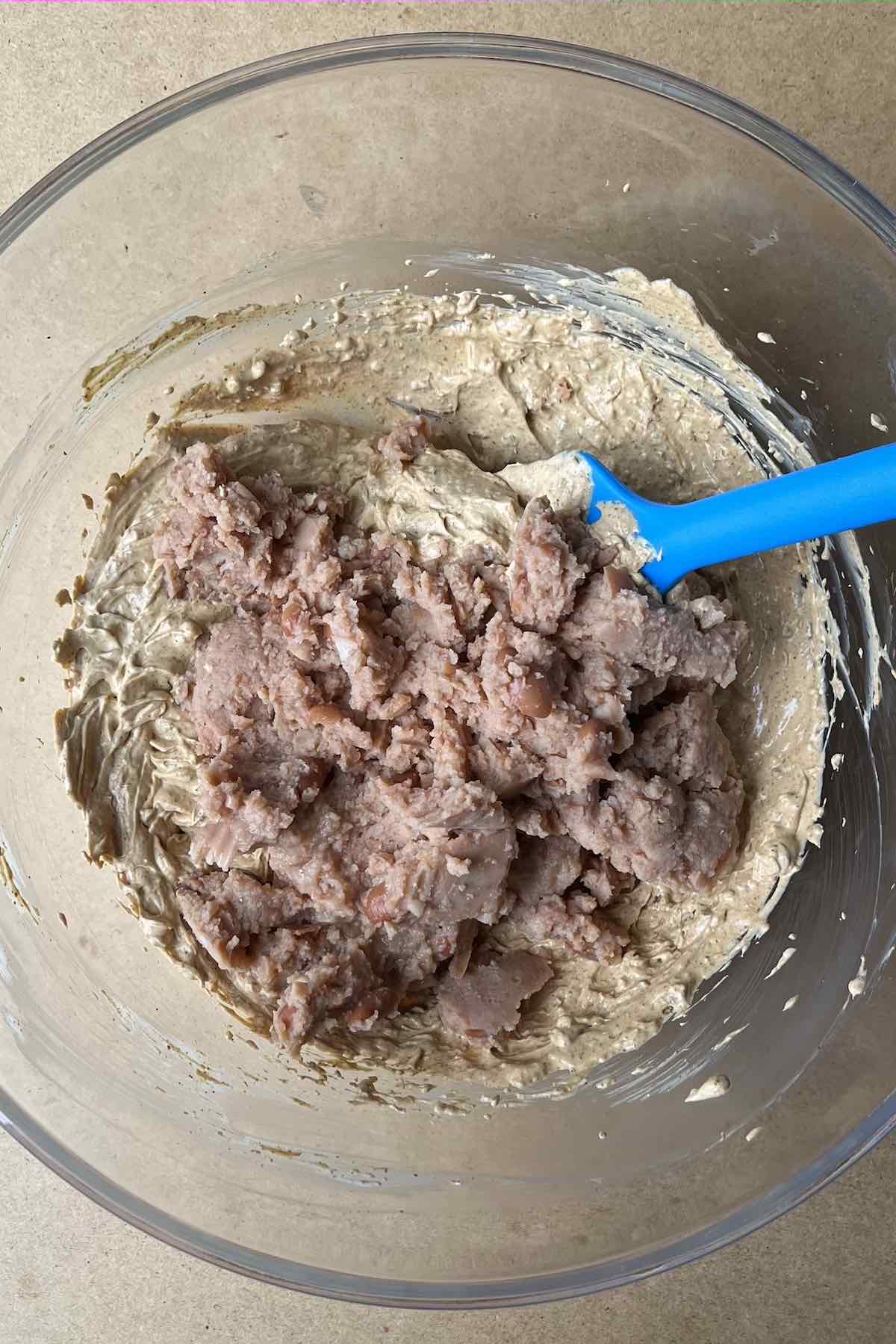 Sour cream, cream cheese, taco seasoning blended with refried beans on top in a bowl.