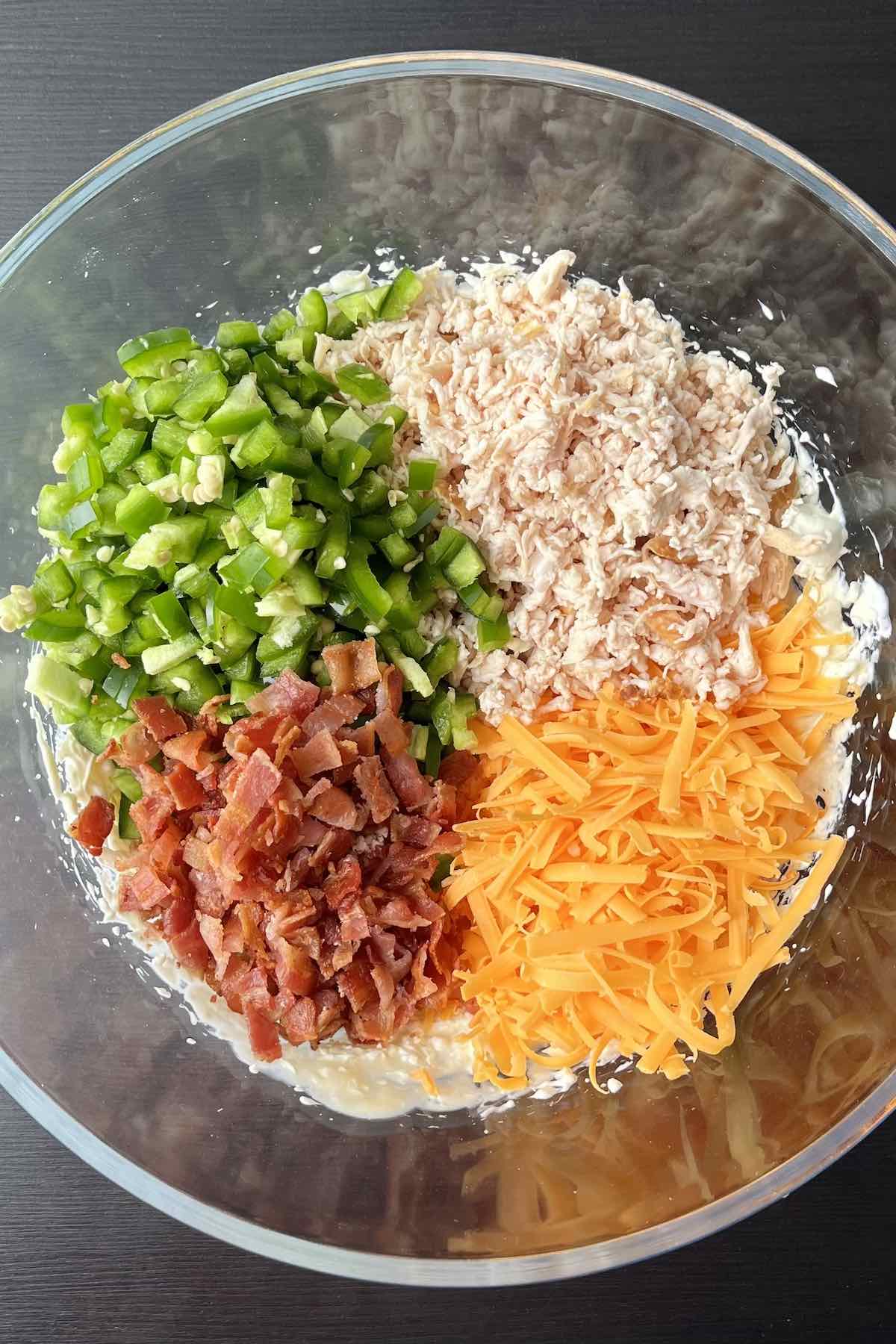 Diced green pepper, bacon pieces, shredded rotisserie chicken, and shredded cheddar cheese added to the bowl of other ingredients.