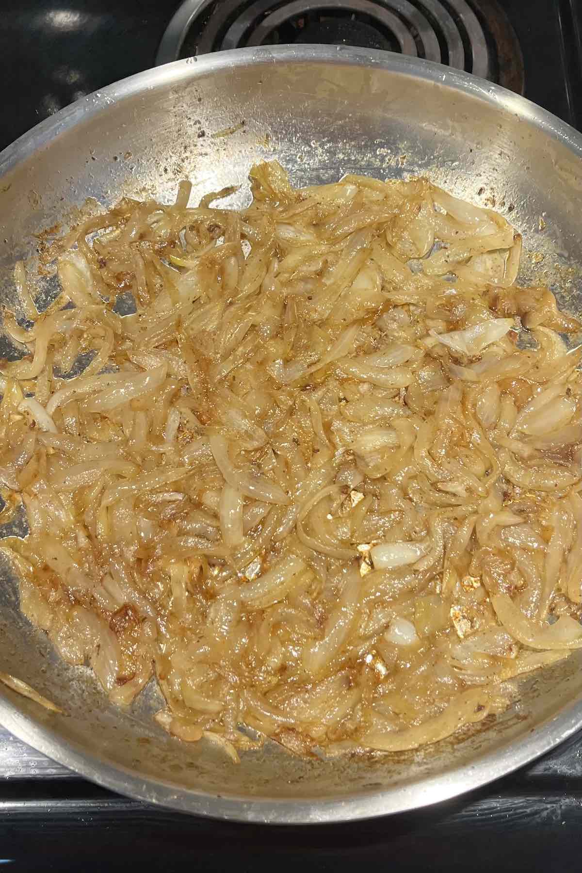 Sliced onions cooked and caramelized on a frying pan.