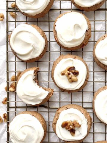 Carrot cake mix cookies with cream cheese icing scattered on a cooling rack with chopped walnuts sprinkled around them.