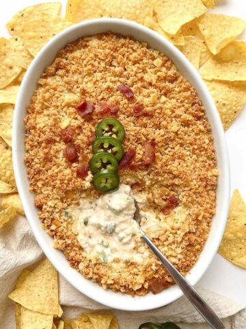 Chicken and bacon jalapeno popper dip in a white oval baking dish with a metal spoon in it.