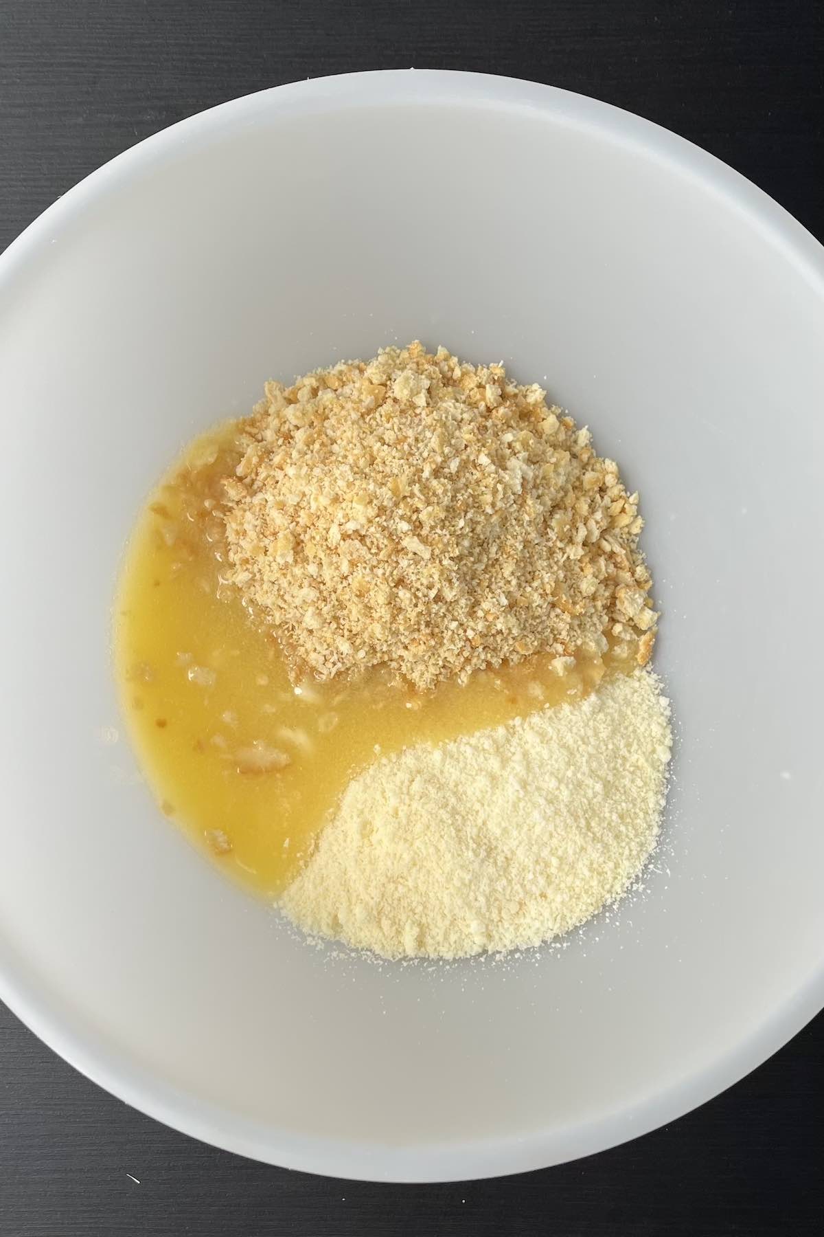 Crushed crackers, melted butter, and parmesan in a bowl.
