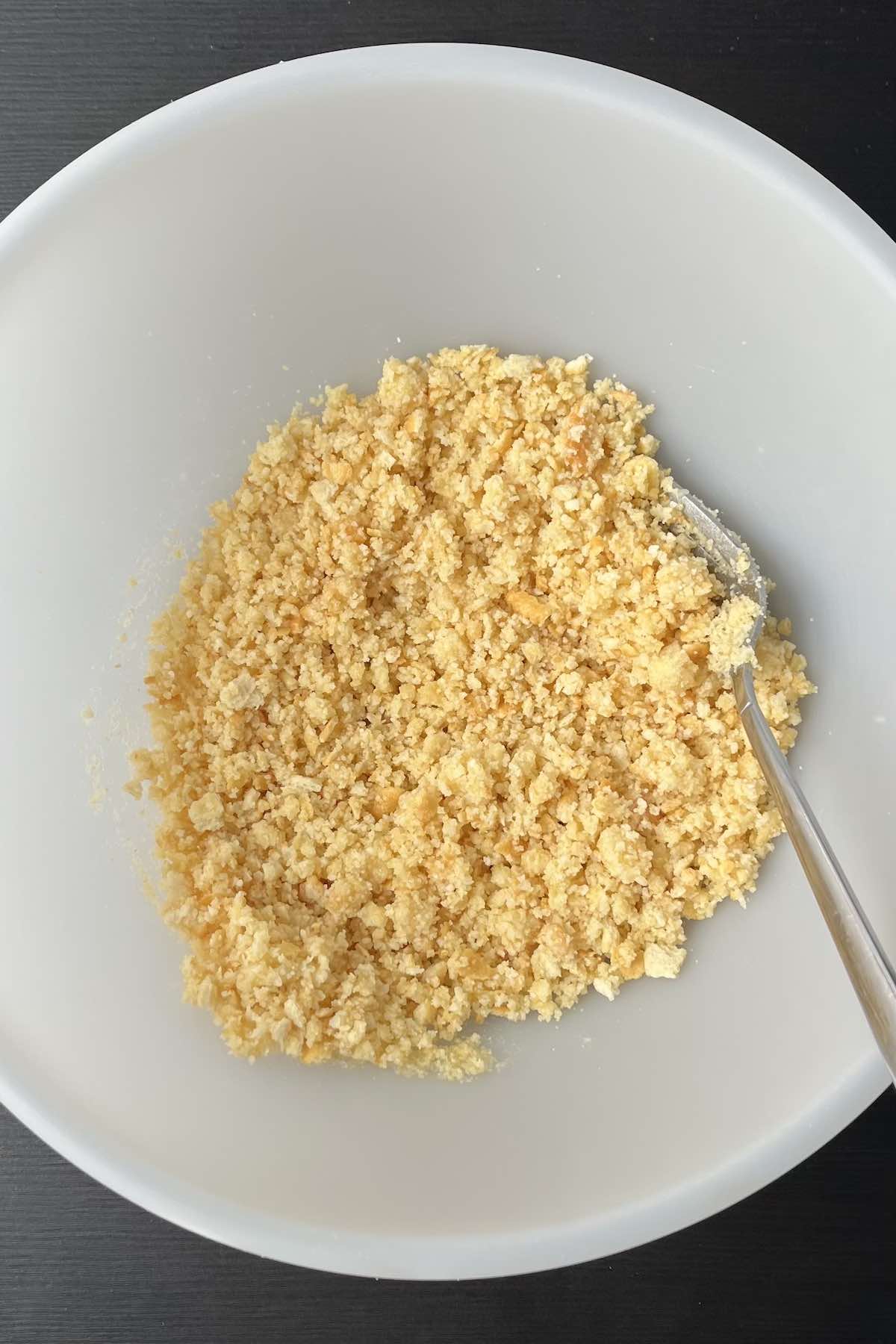 Crushed crackers, melted butter, and parmesan mixed in a bowl.