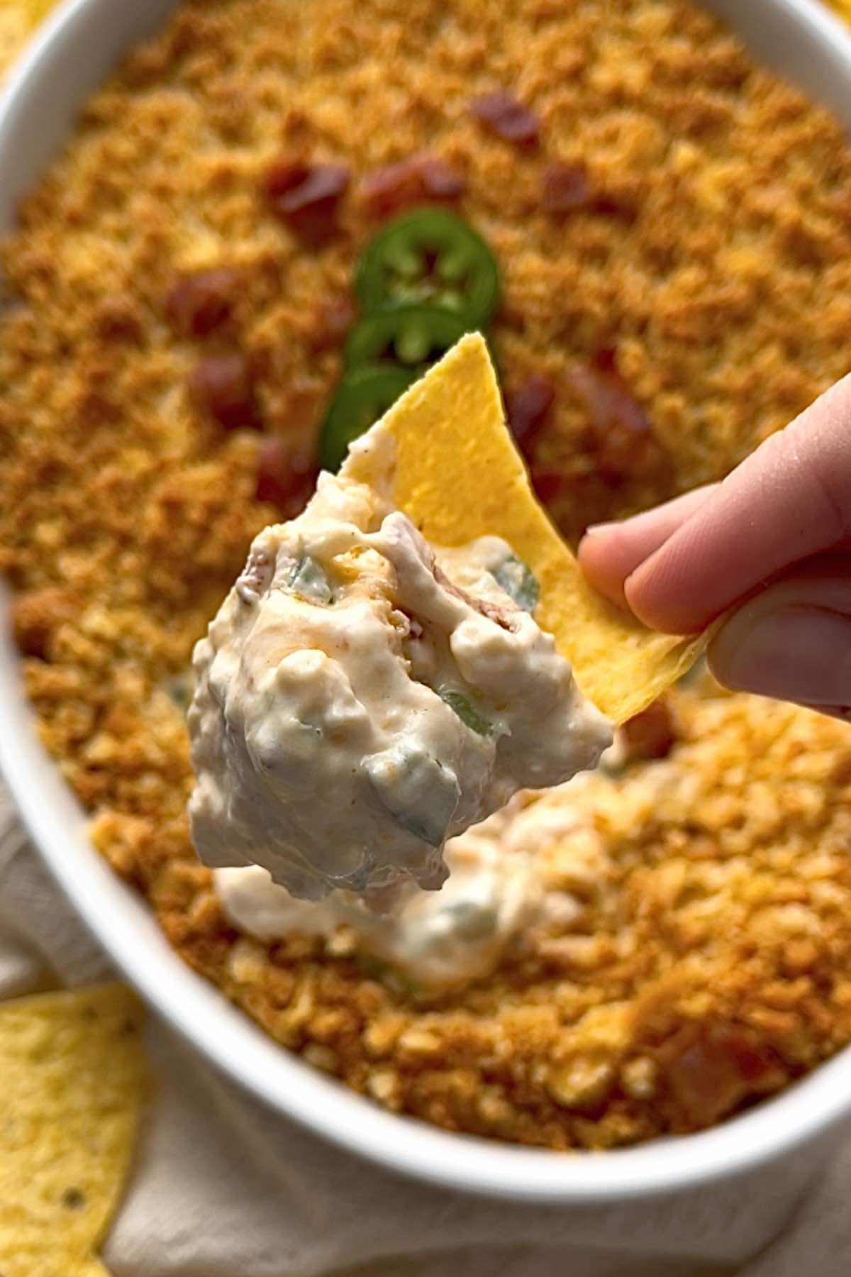 Chicken and bacon jalapeno popper dip on a tortilla chip with a hand holding it.