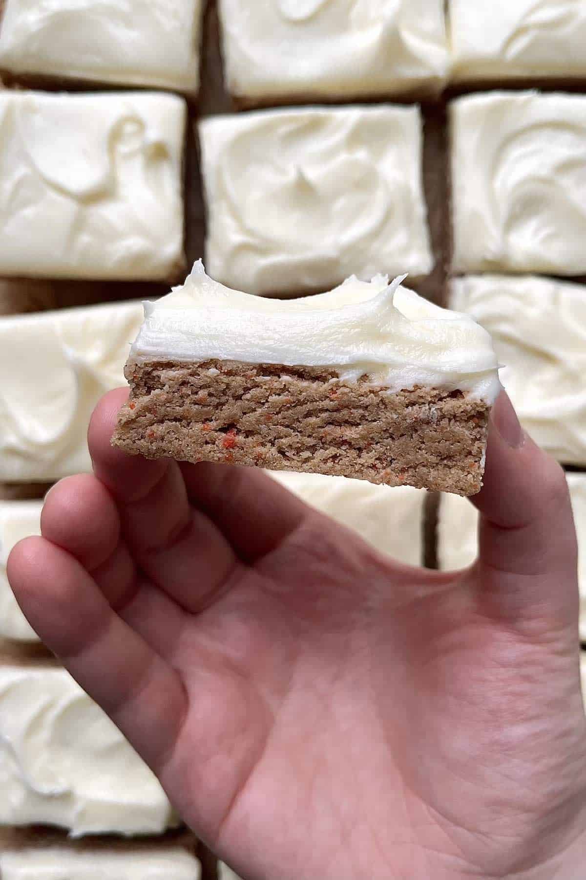 Hand holding a carrot cake bars with cream cheese frosting.