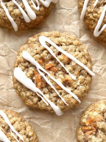 Carrot cake oatmeal cookies with cream cheese glaze scattered on a brown piece of parchment paper.