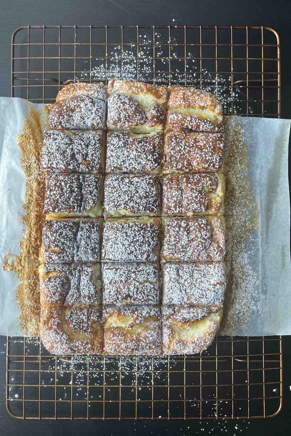 Cooled lemon bars cut into squares on a cooling rack and dusted with icing sugar.