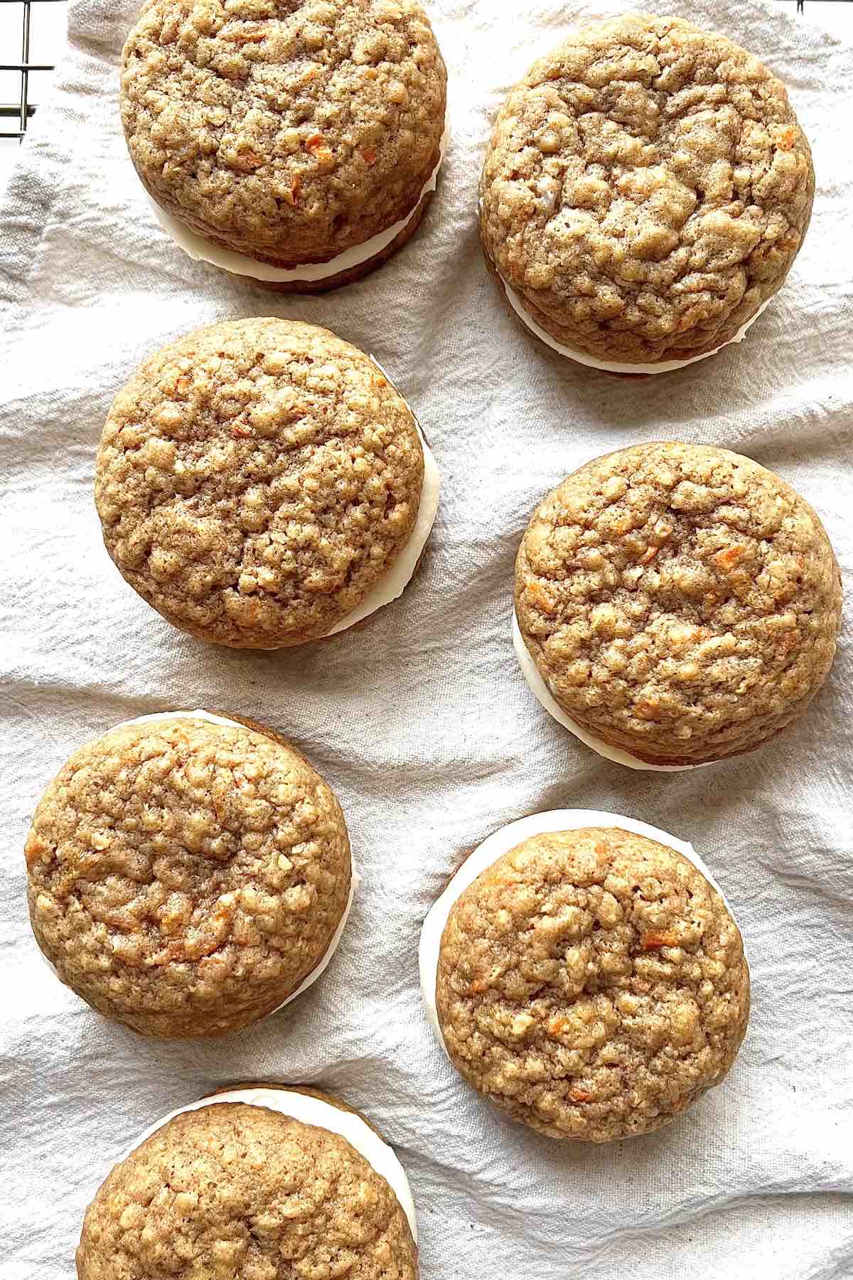 Carrot cake sandwich cookies scattered on a beige linen towel.