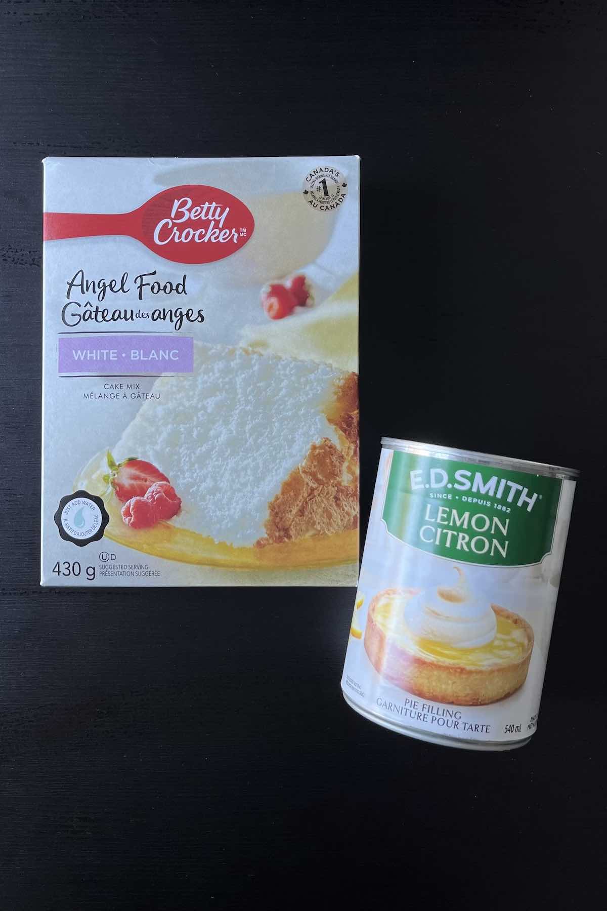 Ingredients on a table including a box of angel food cake mix and can of lemon pie filling. 