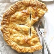 Apple pie with puff pastry in a glass pie dish with a few slices taken out of it.