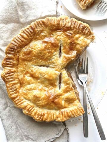 Apple pie with puff pastry in a glass pie dish with a few slices taken out of it.