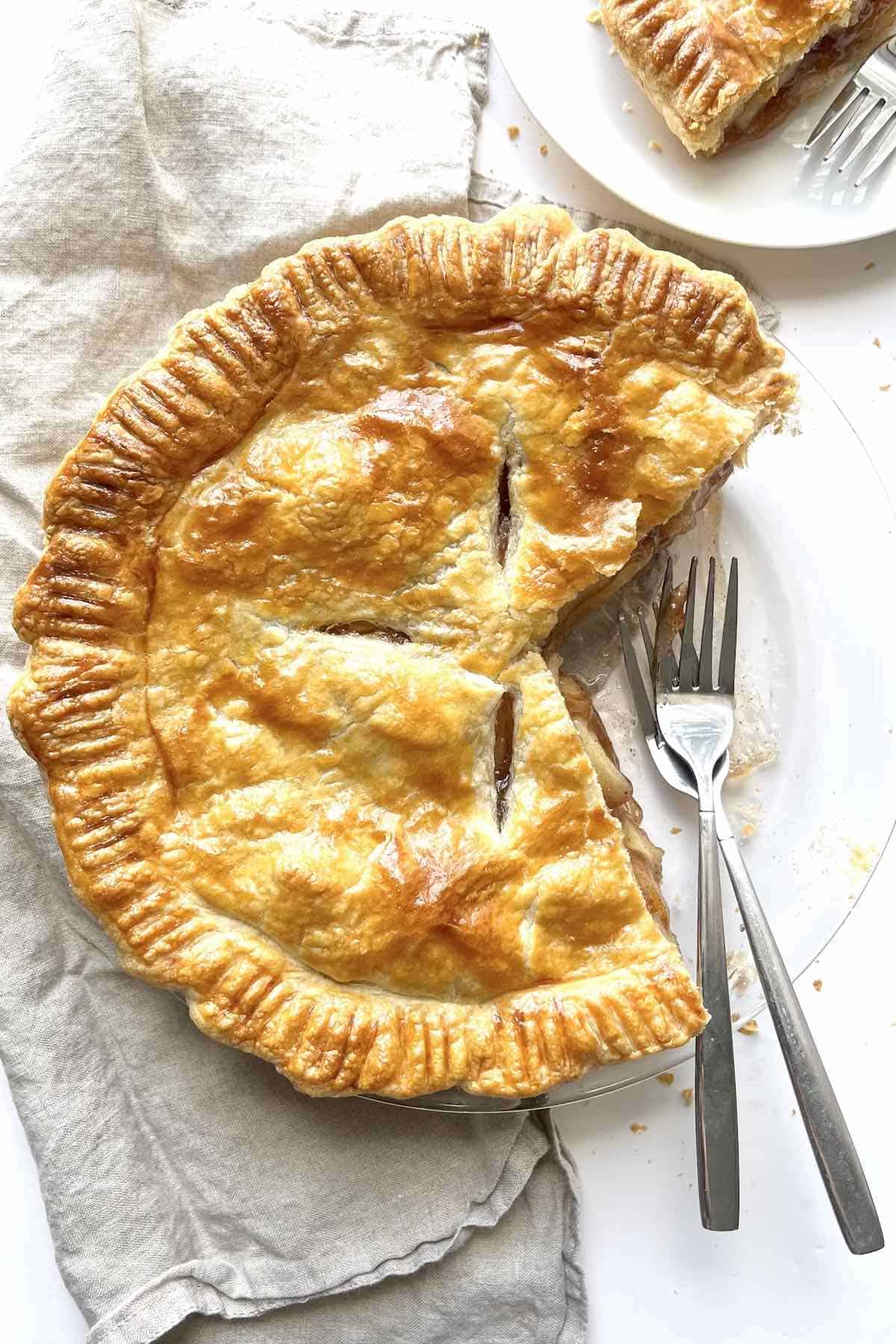 Apple pie with puff pastry in a glass pie dish with a few slices taken out of it.