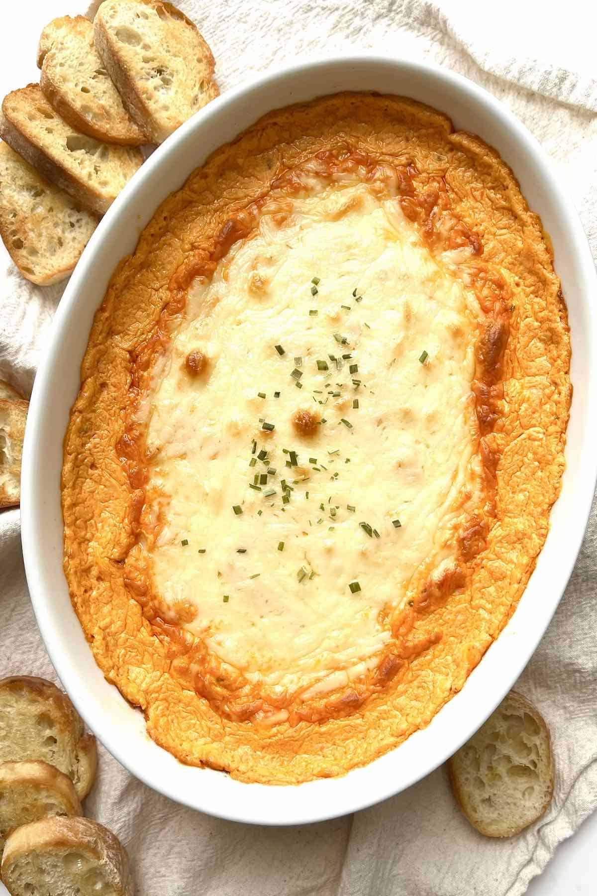 Buffalo crab dip in a white oval baking dish with toasted baguette slices next to it.