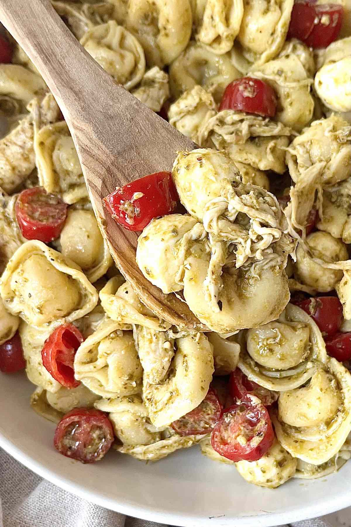 Wooden spoon with a scoop of chicken tortellini pasta salad on it.