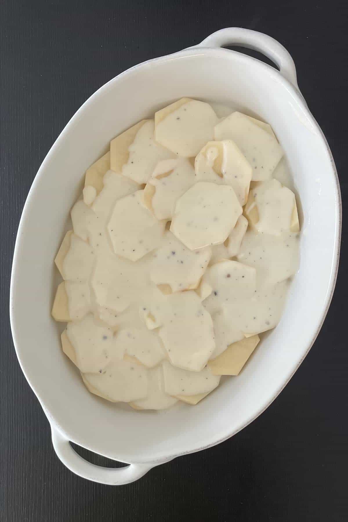 Roux distributed over potatoes in a white baking dish.