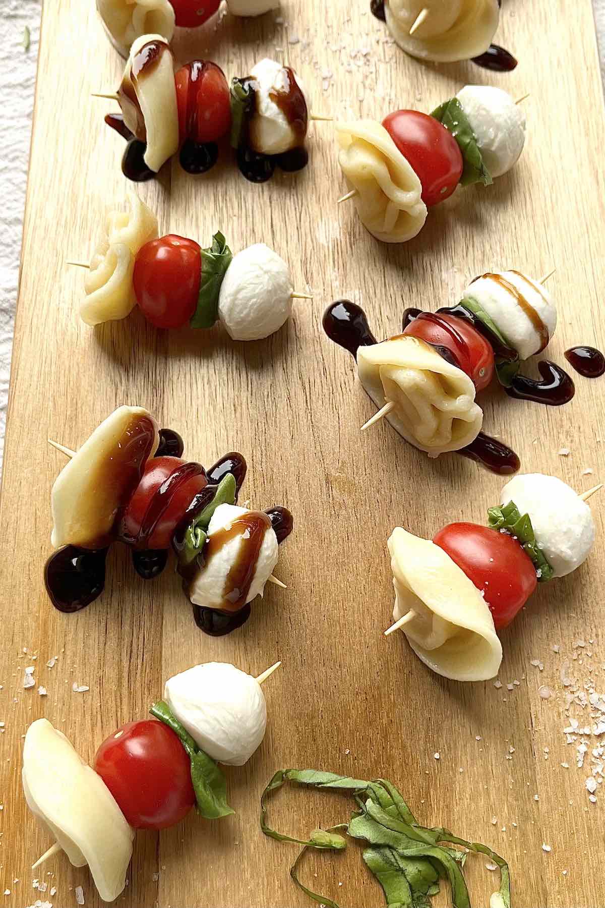 Tortellini caprese skewers scattered on a wooden serving board.