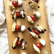 Tortellini caprese skewers scattered on a wooden serving board.