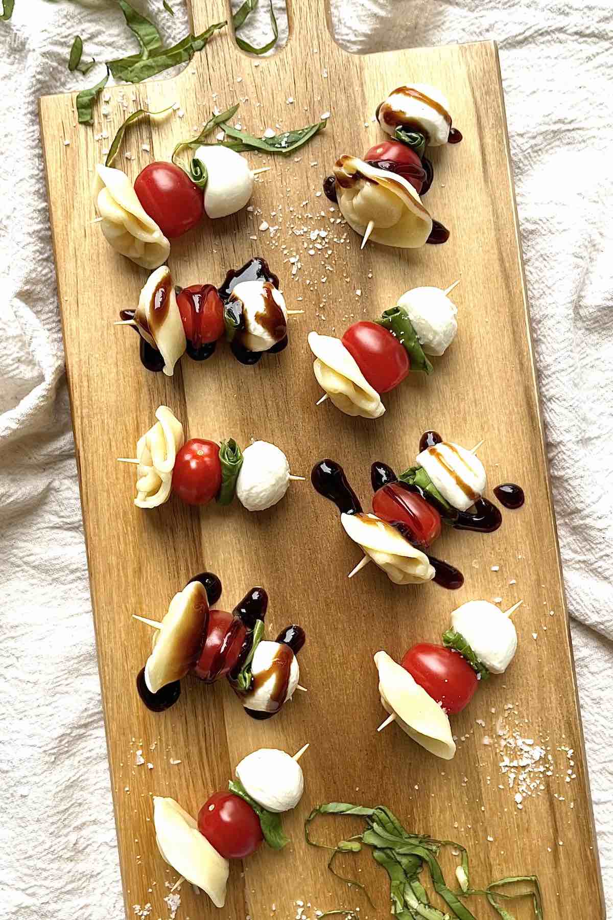 Tortellini caprese skewers scattered on a wooden serving board.