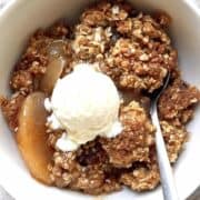 Apple crisp with canned apples in a white bowl topped with a scoop of vanilla ice cream.