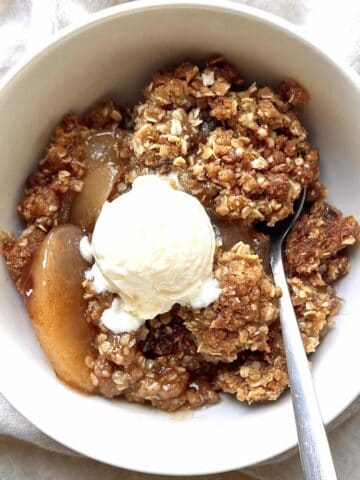 Apple crisp with canned apples in a white bowl topped with a scoop of vanilla ice cream.