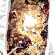 Berry cobbler in a white casserole dish topped with a scoop of vanilla ice cream.