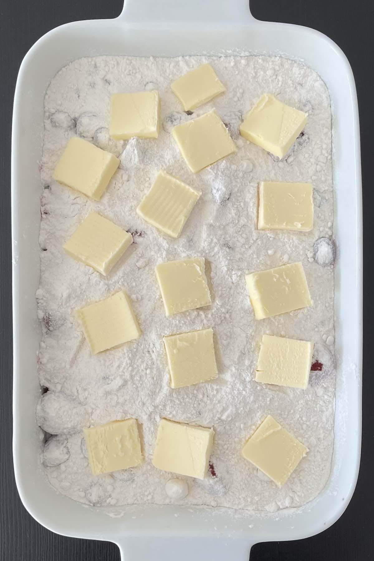 Cake mix and butter slices distributed over the berry mixture in a casserole dish.