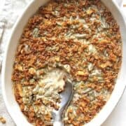 Creamy green bean casserole in a white oval casserole dish with a metal serving spoon in it.