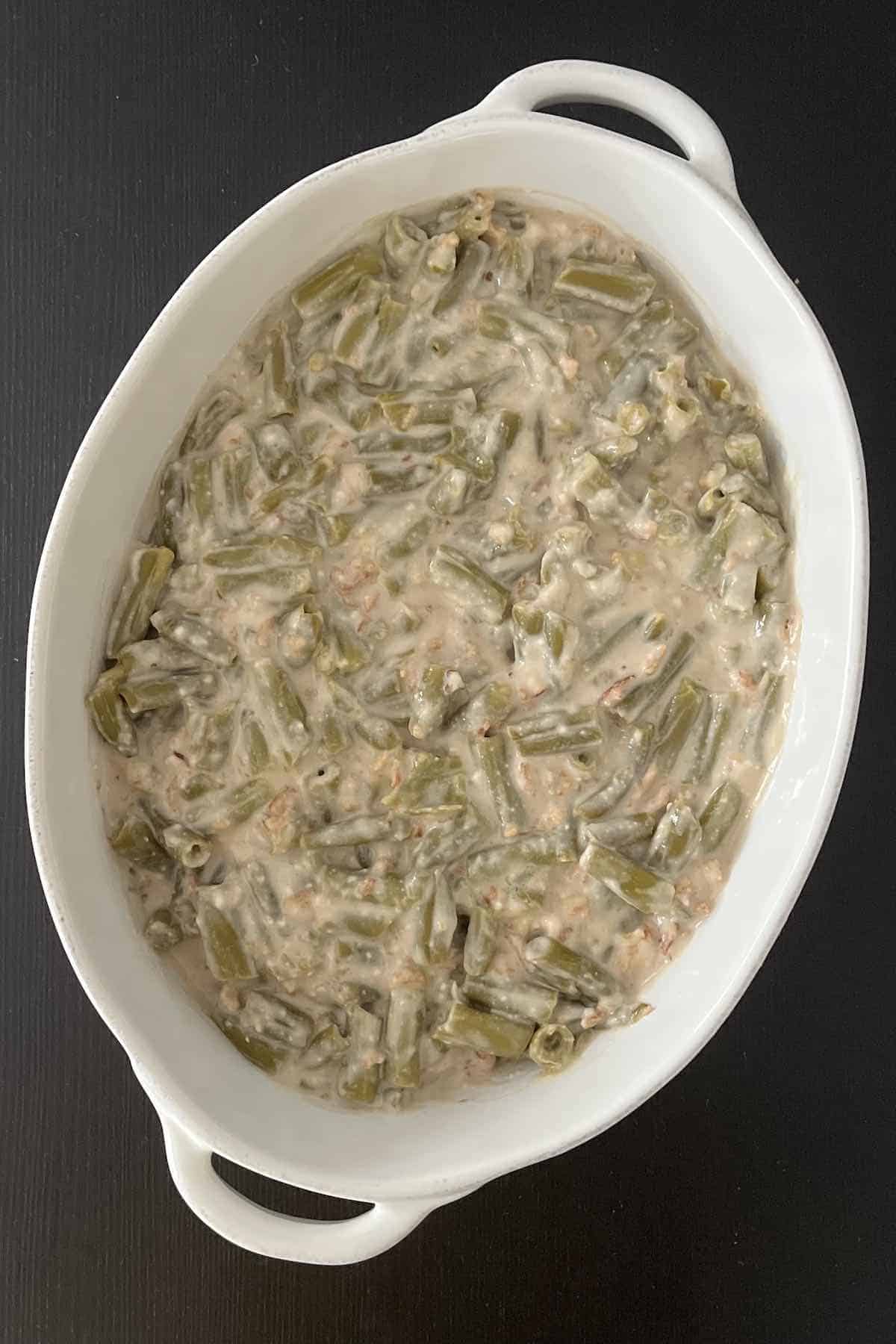 Ingredients including green beans, mushroom soup, milk, soy sauce, french fried onions, and salt and pepper mixed in a casserole dish.