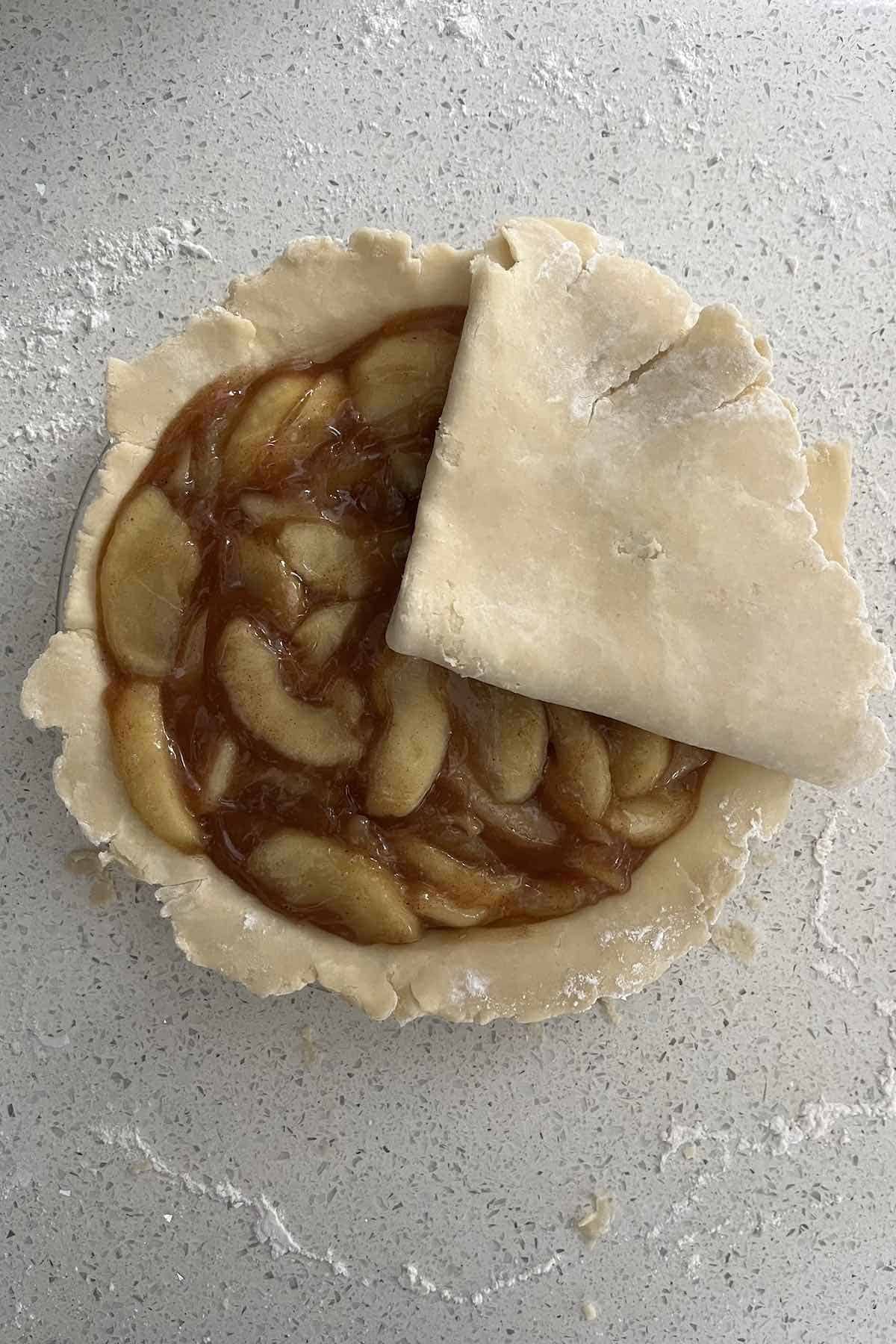 Top pie dough in quarters transferred on top of the pie.