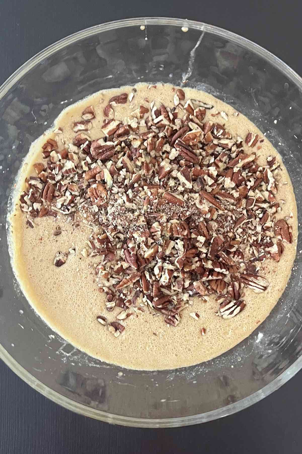 Eggs, brown sugar, corn syrup, butter, and vanilla mixed in a bowl with pecans added to it.