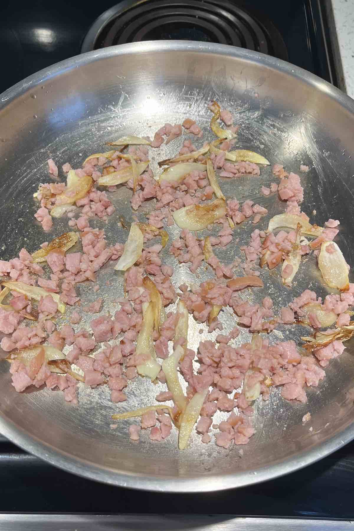 Onions and ham frying in a pan.