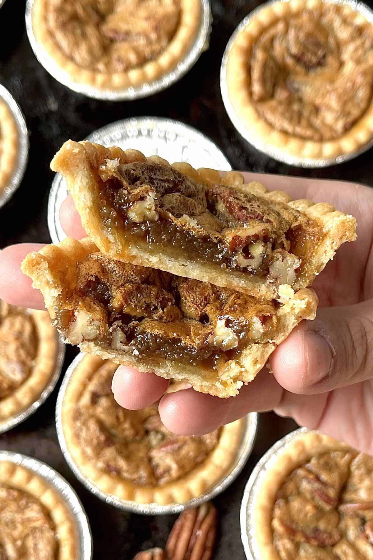 Hand holding two halves of a pecan butter tart showing the gooey centre.