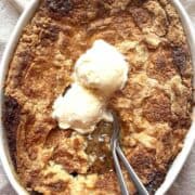 Pecan pie cobbler with cake mix in a white oval baking dish topped with two scoops of vanilla ice cream.