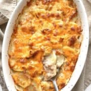 Cheesy scalloped potatoes and ham in a white oval casserole dish.