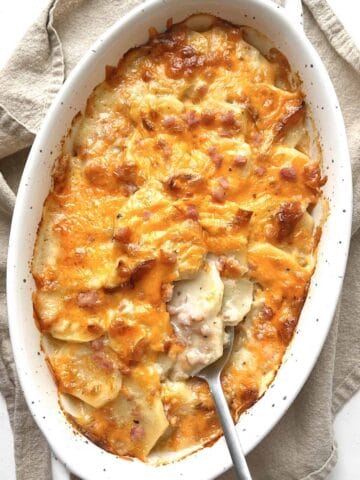 Cheesy scalloped potatoes and ham in a white oval casserole dish.
