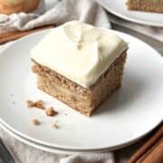 Slice of frosted apple spice cake on a white plate.