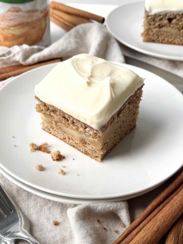 Slice of frosted apple spice cake on a white plate.
