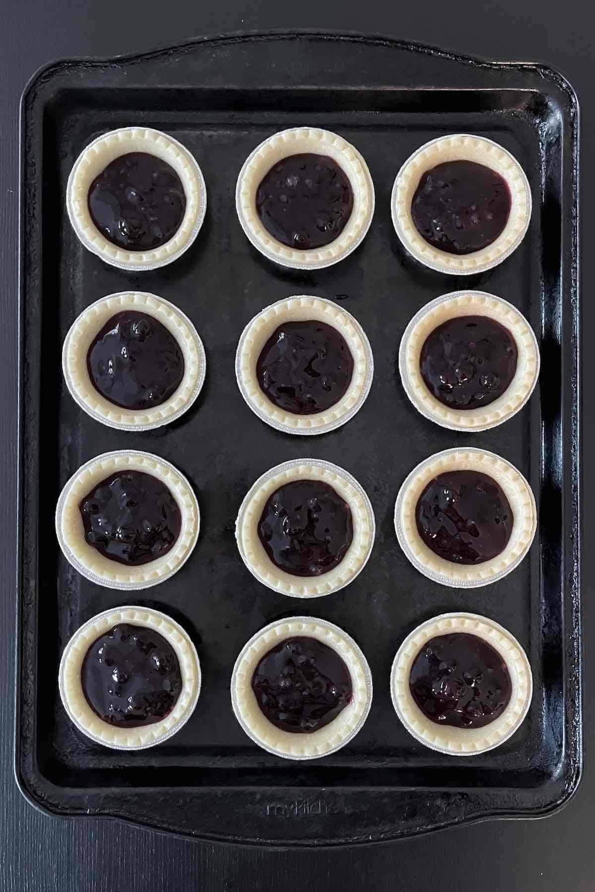 Unbaked blueberry tarts lined on a baking sheet.
