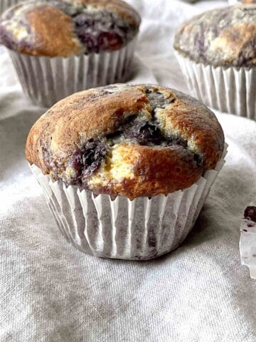 A blueberry muffin on a kitchen linen with more muffins in the background.