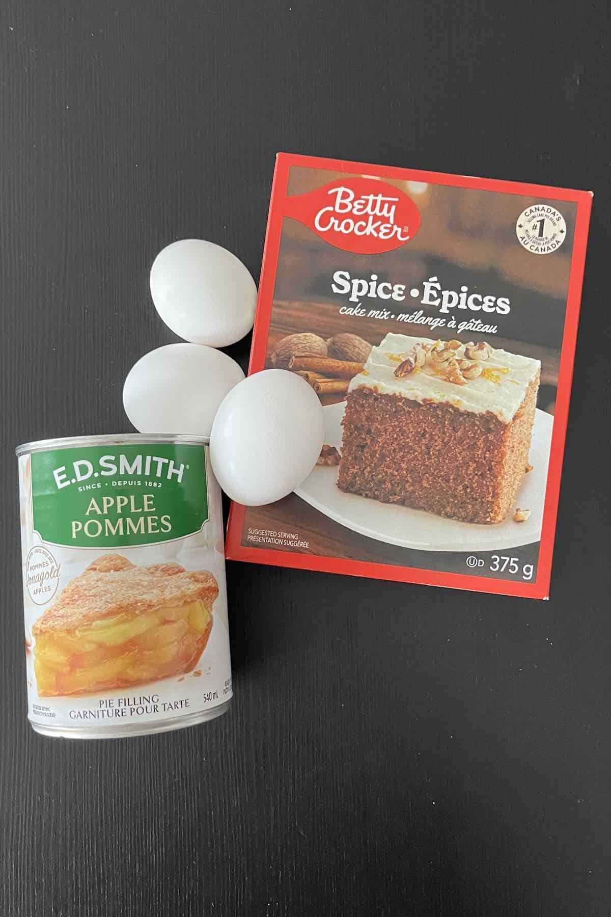 Ingredients on a table including eggs, apple pie filling, and a box of spice cake mix.
